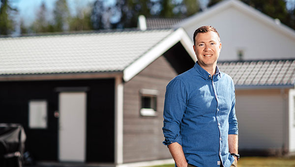 Bild på Mikael Berg i förgrunden och i bakgrunden ett svart hus med ljusgrått tak.