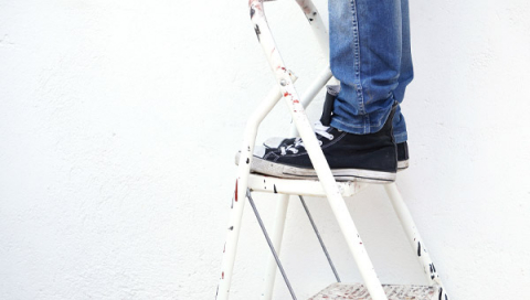 Någon står på en stege med jeans och Converse, endast ben, fötter och stege syns i bild.