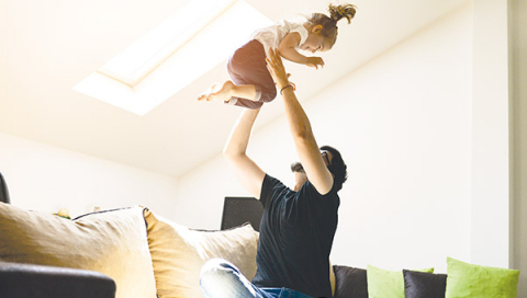 En pappa håller sitt barn upp mot taket, nöjd över att han har ett tak med de bästa garantierna från BMI Sverige.