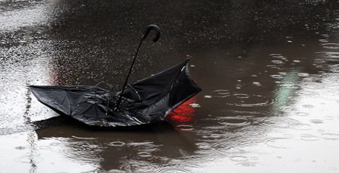 Trasigt paraply ligger i en vattenpöl och det regnar.